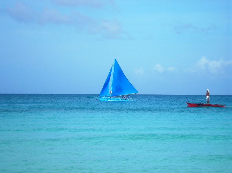 a lone sailboat proudly glides the calm waves of Boracay waters